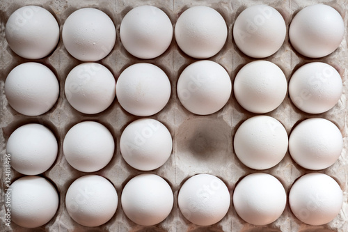 White chicken eggs in a cardboard box with one empty space, background.