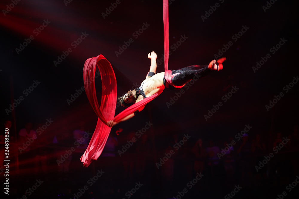 Fototapeta Brazylijski silny seksowny mężczyzna wykonuje występy na powietrznych jedwabiach w czerwonych światłach, upuszcza na powietrznych jedwabiach. Sport szkolenia siłownia i koncepcja stylu życia.