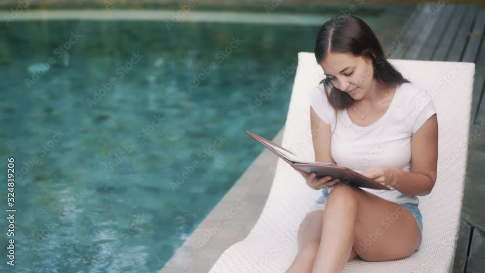 beautiful girl chooses dish in menu near swimming pool beautiful girl chooses dish in menu near swimming pool