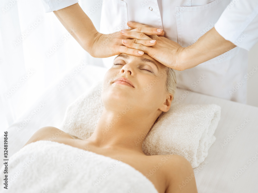 Beautiful blonde woman enjoying facial massage with closed eyes. Relaxing treatment in medicine and spa center concepts