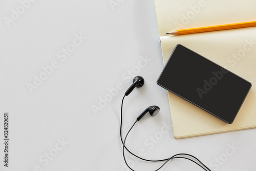 technology and objects concept - earphones, smartphone and notebook with pencil on white background