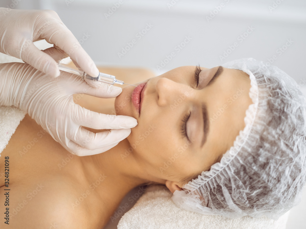 Beautician doing beauty procedure with syringe to face of young brunette woman. Cosmetic medicine and surgery, beauty injections Beautician doing beauty procedure with syringe to face of young brunette woman. Cosmetic medicine and surgery, beauty injections