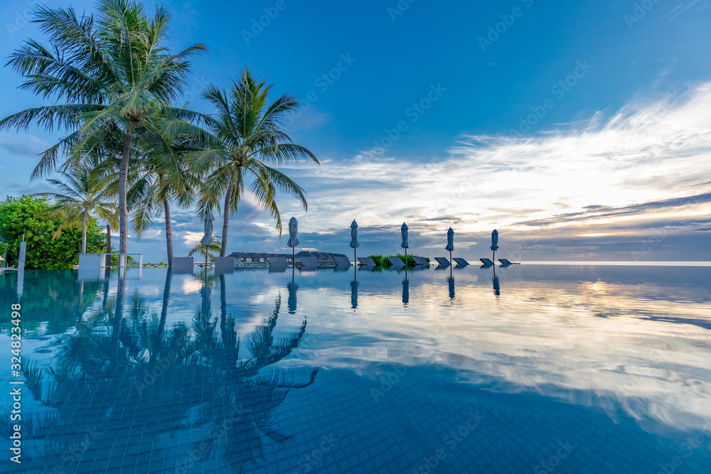 Beautiful poolside and sunset sky. Luxurious tropical beach landscape, deck chairs and loungers and water reflection over the swimming pool. Luxury summer vacation or holiday, hotel resort