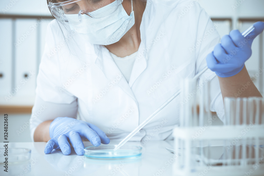 Close-up of professional female scientist in protective eyeglasses making experiment with reagents in laboratory. Medicine and research concept Close-up of professional female scientist in protective eyeglasses making experiment with reagents in laboratory. Medicine and research concept