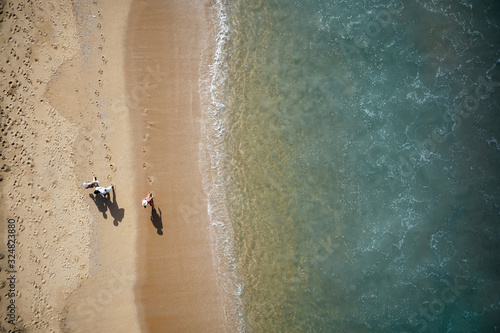 People walking along the beach. Aerial View of Waves and Azure beach with rocks. Kerala, India.