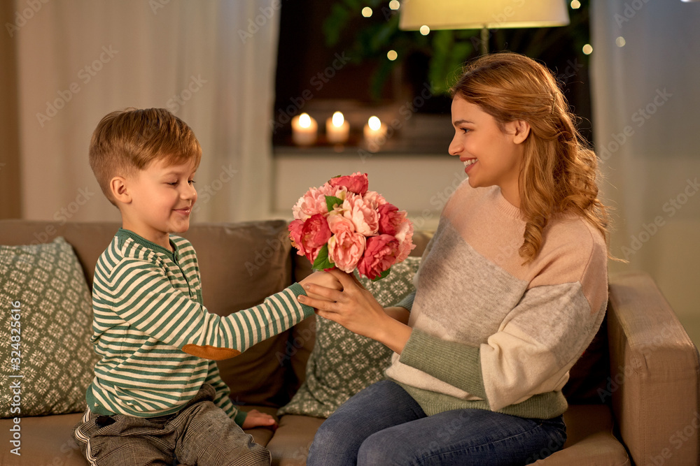 mother's day, holidays and family concept - happy little son giving flowers to his smiling mother at home in evening mother's day, holidays and family concept - happy little son giving flowers to his smiling mother at home in evening