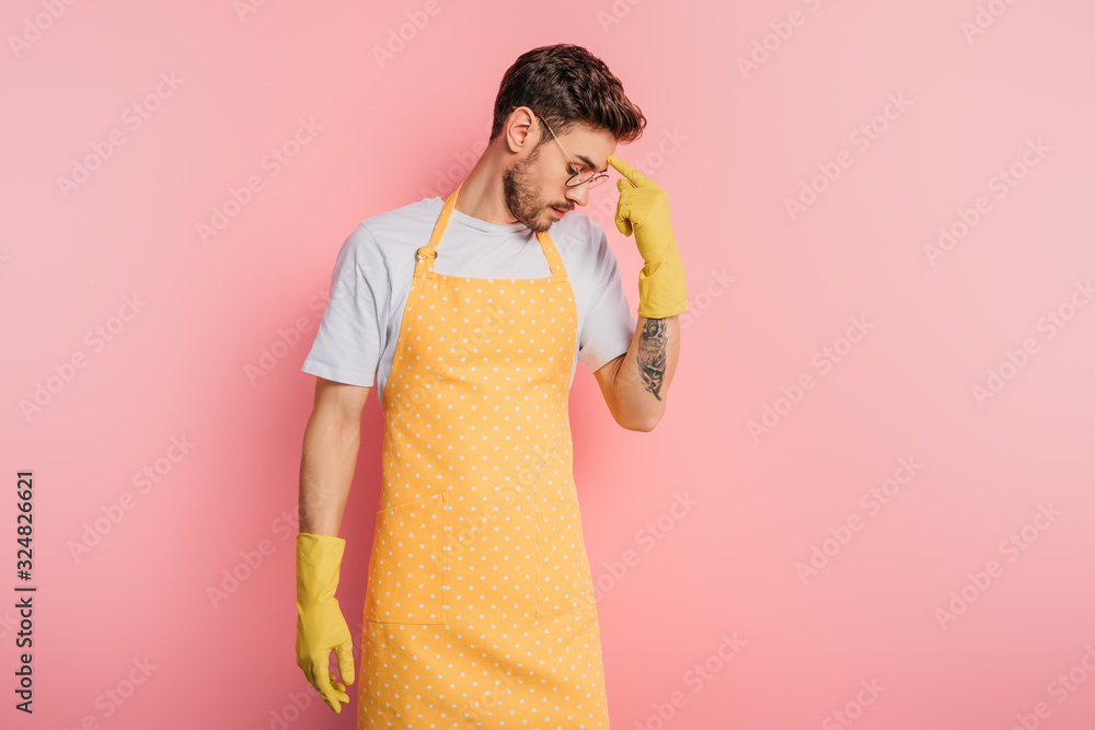 thoughtful young man in apron and rubber gloves touching forehead with finger on pink background thoughtful young man in apron and rubber gloves touching forehead with finger on pink background