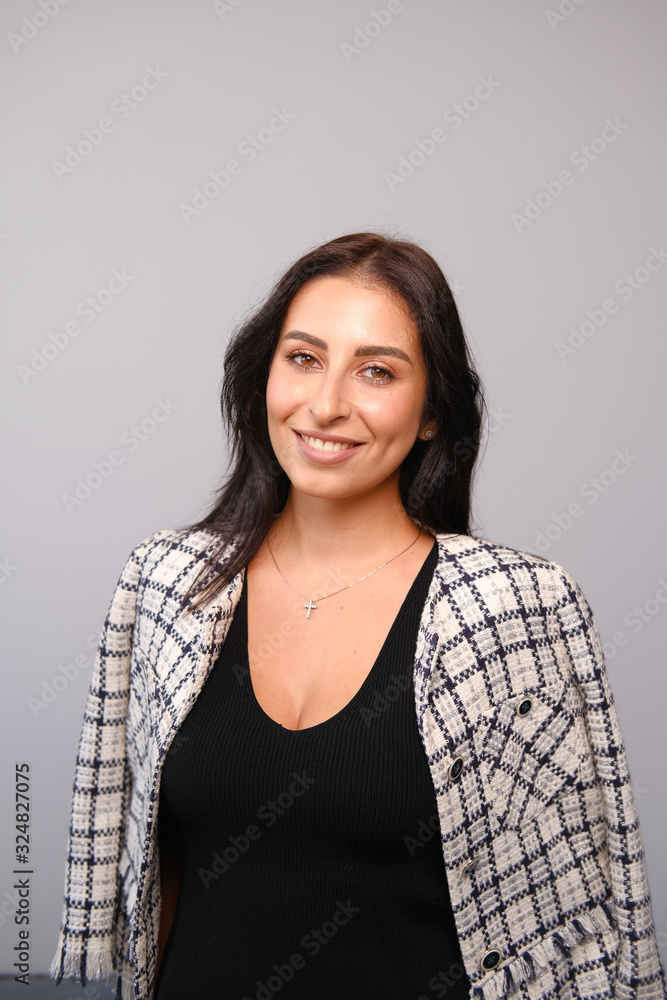 Fototapeta premium Portrait of a smiling mid-aged business woman with dark hair and brown eyes in glasses in jacket against a light wall