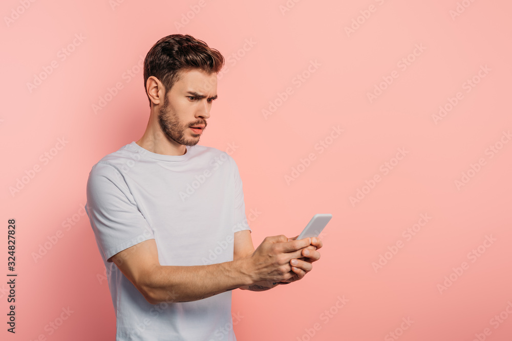 shocked young man chatting on smartphone on pink background shocked young man chatting on smartphone on pink background