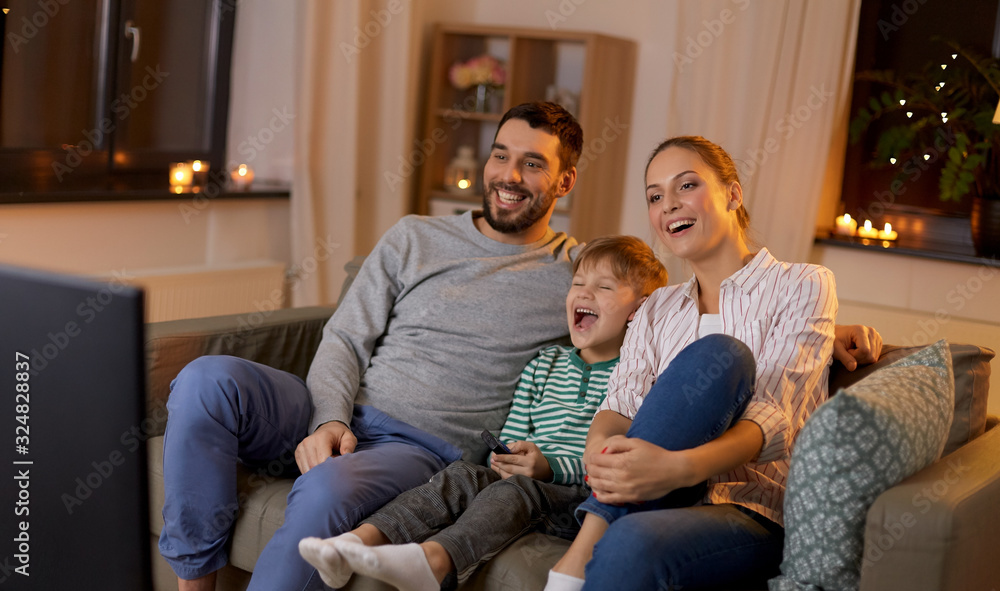 family, leisure and people concept - happy smiling father, mother and little son with remote control watching something funny on tv at home at night