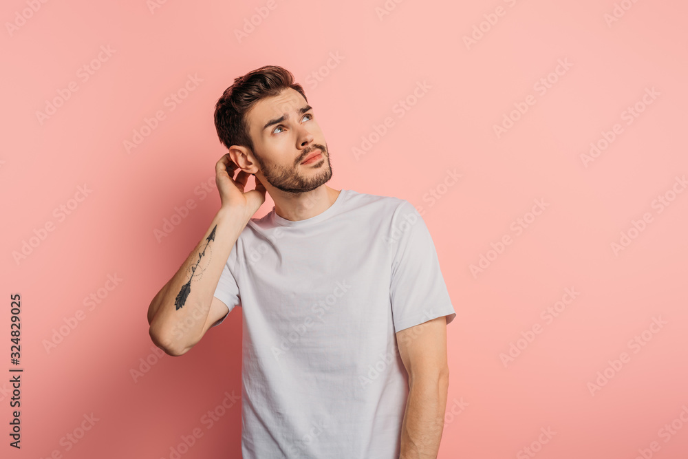 dreamy young man touching head and looking up on pink background dreamy young man touching head and looking up on pink background