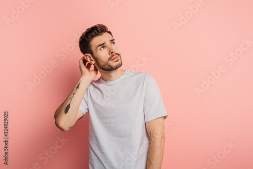 dreamy young man touching head and looking up on pink background