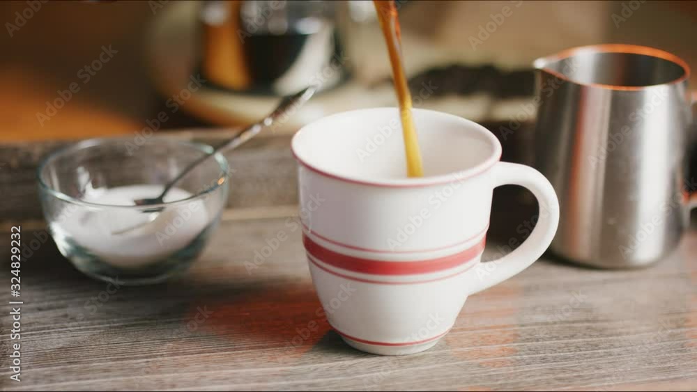 Pouring coffee into a red stripe mug in real time with a slow dolly move. Pouring coffee into a red stripe mug in real time with a slow dolly move.