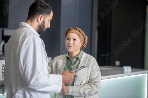 Tall male young doctor in a white robe talking to a female patient