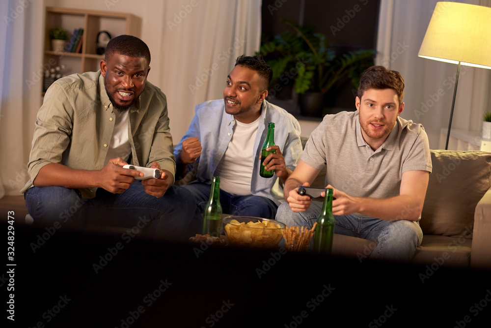 friendship, technology and leisure concept - smiling male friends with gamepads and beer playing video game at home at night friendship, technology and leisure concept - smiling male friends with gamepads and beer playing video game at home at night