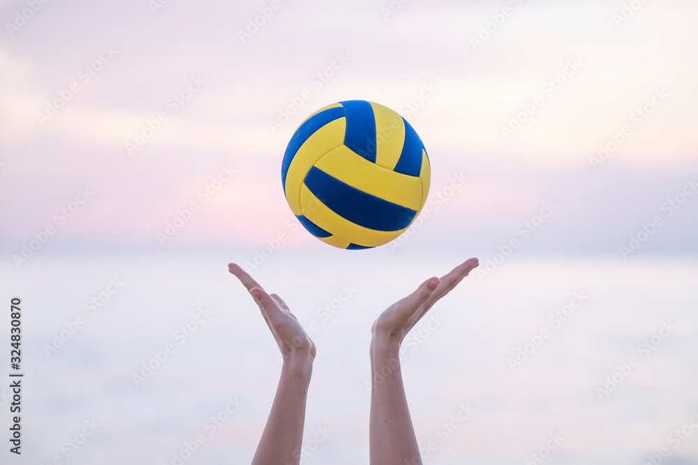 female hands throw up volleyball ball, behind sea on sunset time, summer. Photo is ideal for advertising, poster and wallpaper