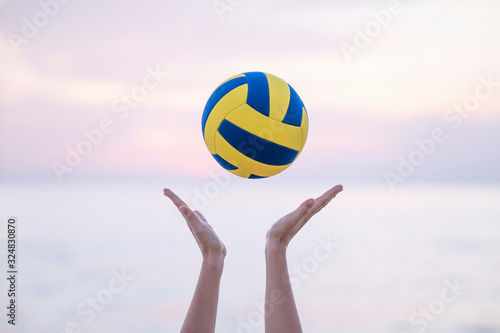 female hands throw up volleyball ball, behind sea on sunset time, summer. Photo is ideal for advertising, poster and wallpaper