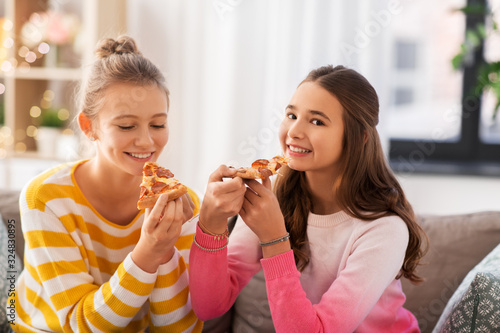 people, food and friendship concept - happy teenage girls eating pizza at home