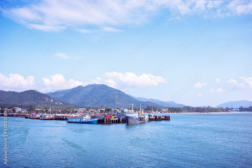 Ferry landing pier with fishing ship. Landscape with island Samui, blue sea and sky.