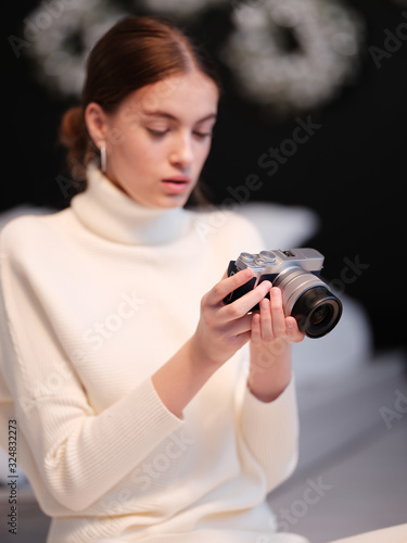 Hobby and freelance concept. Girl photographer holds a mirrorless camera in her hands. Closeup portrait of a funny young girl. 