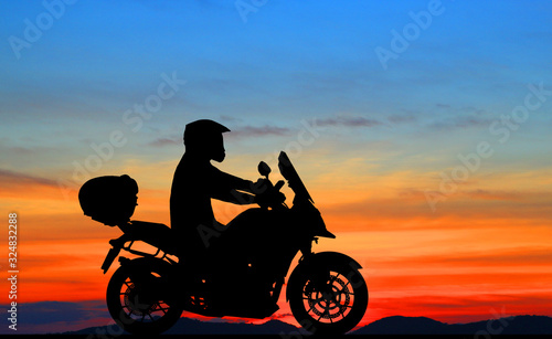 Silhouette biker with his motorbike beside the natural lake and beautiful sunset sky. © rathchapon