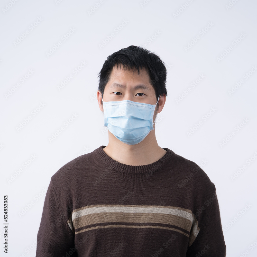 Young Asian man portrait, feeling sick, wearing a surgical blue face mask to prevent infection, air pollution isolated on white background, cut out. Young Asian man portrait, feeling sick, wearing a surgical blue face mask to prevent infection, air pollution isolated on white background, cut out.