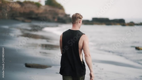 tall man walks along beach with volcanic sand against ocean photo