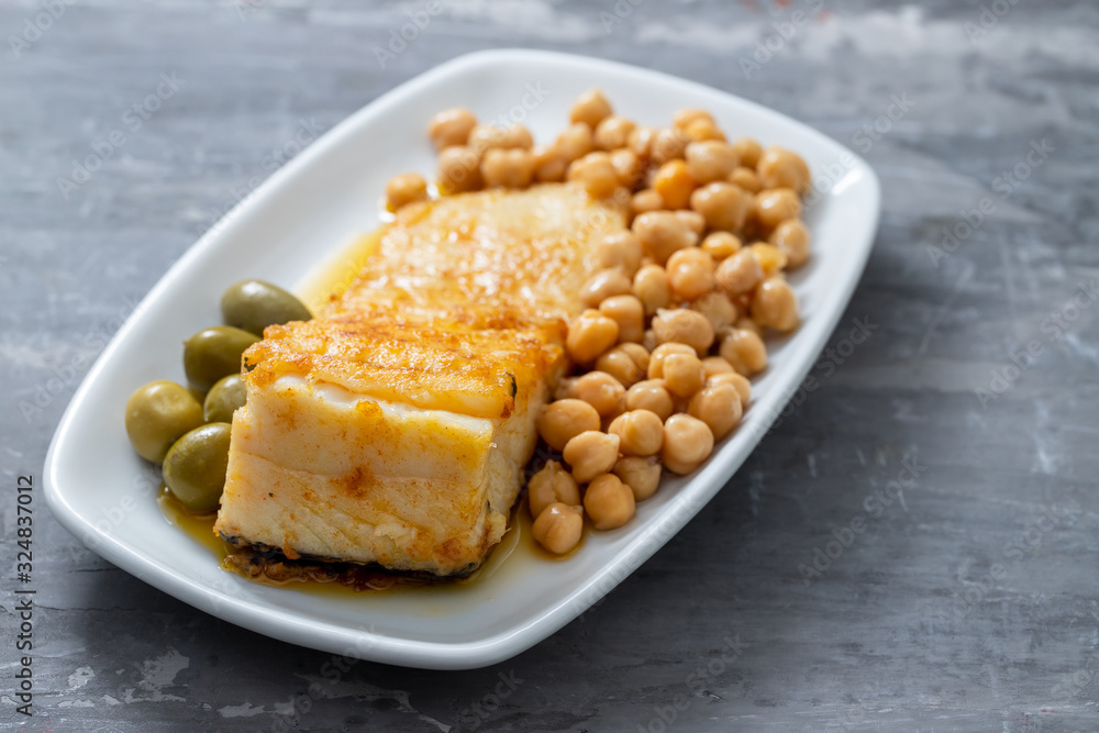 fried cod fish with chick pea and olives on white dish on ceramic background fried cod fish with chick pea and olives on white dish on ceramic background
