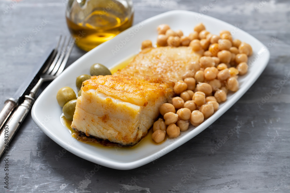 fried cod fish with chick pea and olives on white dish on ceramic background fried cod fish with chick pea and olives on white dish on ceramic background