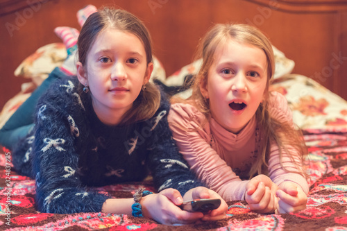 Two happy girls watching tv or movie. A horizontal photo of two young pretty smiling sisters lying on bed and watching their favourite serials