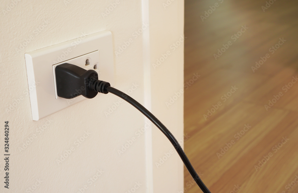 black plug of electrical appliance or device is plugging in the electric socket on white wall, power saving or cost reduction concept