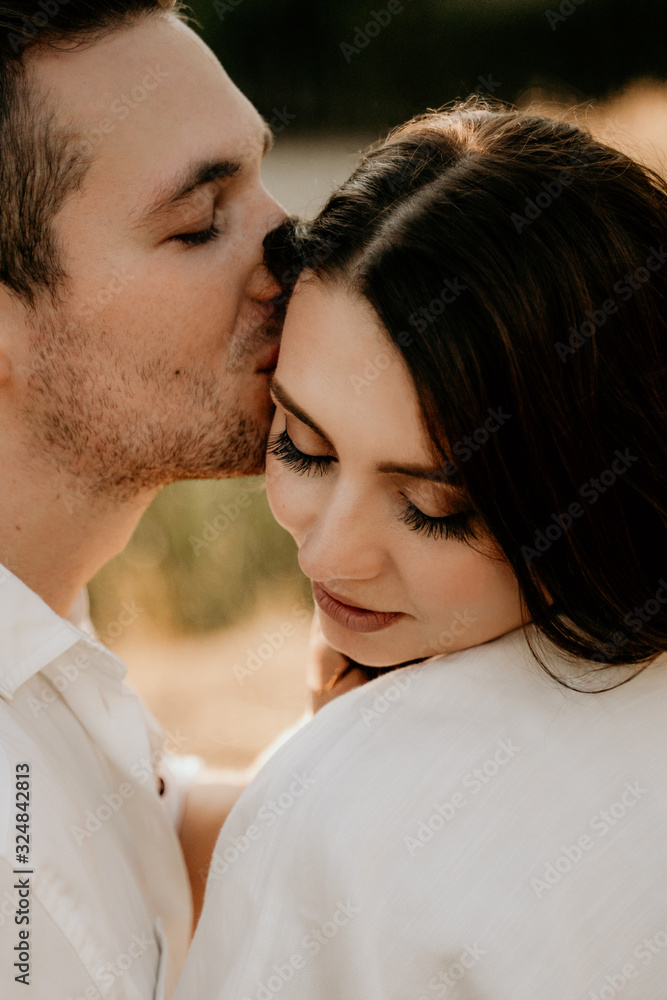 Loving couple hugging and kissing at sunset in summer. Brunette girl in a light dress. Love story. Loving couple hugging and kissing at sunset in summer. Brunette girl in a light dress. Love story.