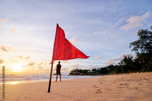 Beautiful sunset on tropical sand beach with red riscue flag. Man enjoying sea view.