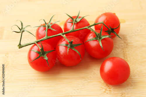 Beautiful red tomatoes on a green branch on a light wooden background and next to one tomato. Selective focus on vegetables. The view from the top.