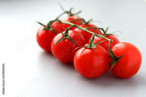 Red delicious fresh cherry tomatoes on a green branch on a light background. The branch with the tomatoes. Selective focus on tomatoes and greens. Healthy vegetables. Vegetarianism. Copy space