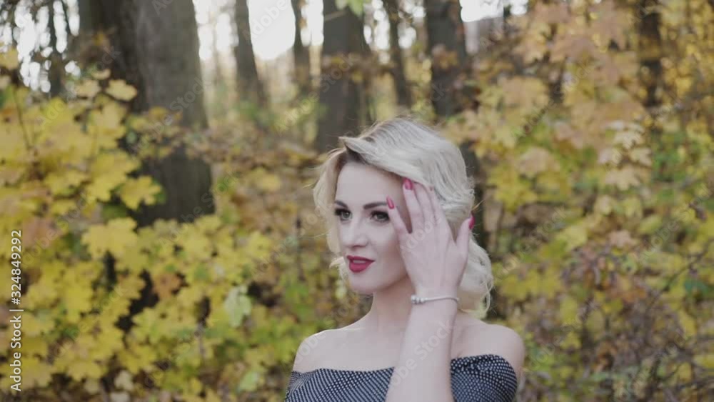 Portrait of cute lady lightly smiles and corrects hairstyle in autumn park Portrait of cute lady lightly smiles and corrects hairstyle in autumn park