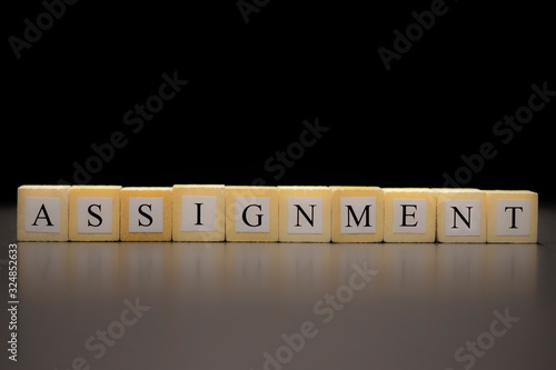 Canvas Print The word ASSIGNMENT written on wooden cubes isolated on a black background