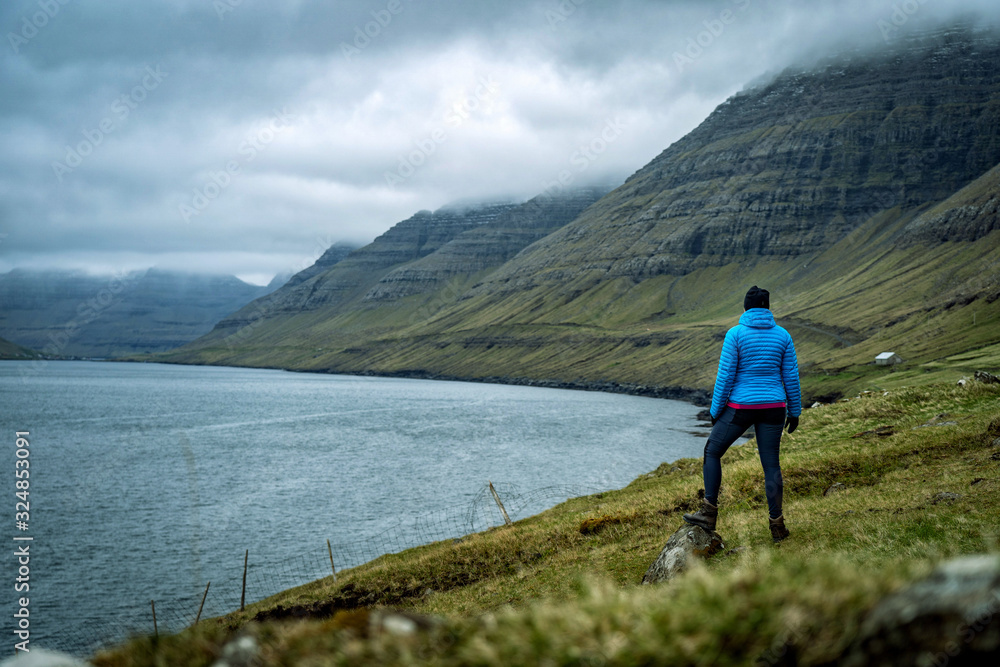 Female traveler standing at top of mountain and enjoying spectacular view over Faroe Islands fjords.