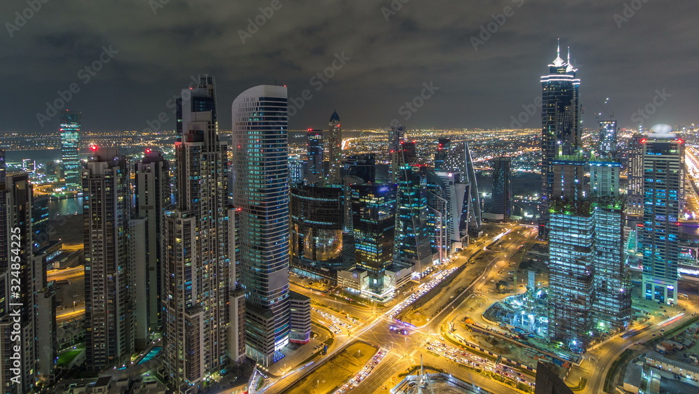 Fototapeta premium Dubai Business Bay wieże oświetlone w nocy timelapse. Widok z dachu niektórych drapaczy chmur i nowych wież w budowie.