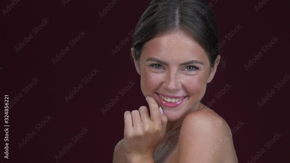 A smiling young woman is sending an air kiss to the camera isolated over dark red background A smiling young woman is sending an air kiss to the camera isolated over dark red background