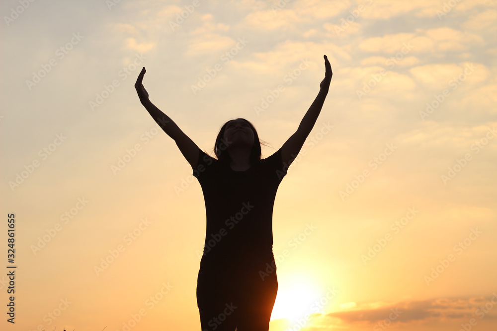 woman silhouette arms up to the sunset feeling happy and freedom.