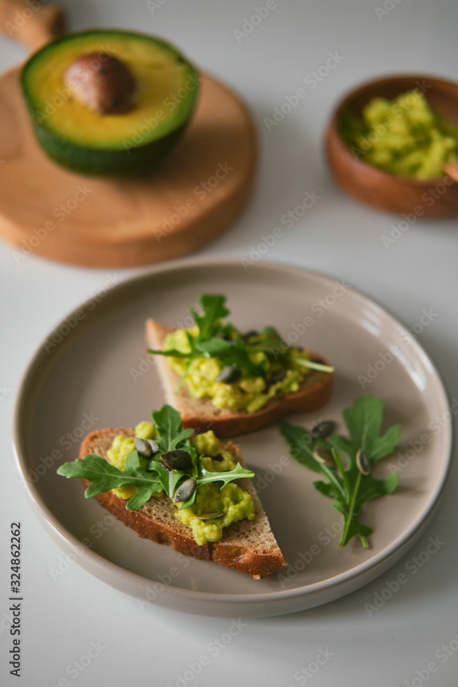 Toast with avocado, arugula on a plate and avocado or wooden board in the shape of deer antlers. Bowl with guacamole