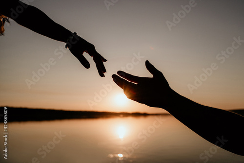 Young couple is embracing in the water on Sunset. Two silhouettes of hands against the sun. Romantic love story.