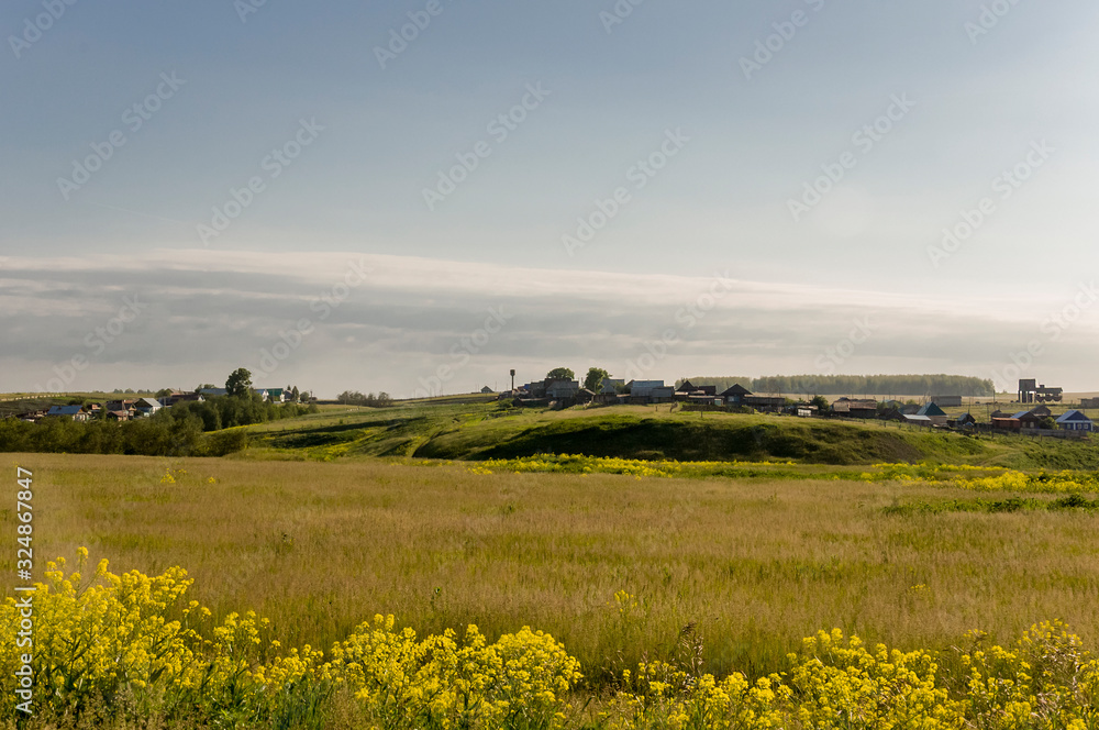 Light white clouds in the warm summer sky over village with small houses far away in the fields. Travelling. People living Light white clouds in the warm summer sky over village with small houses far away in the fields. Travelling. People living