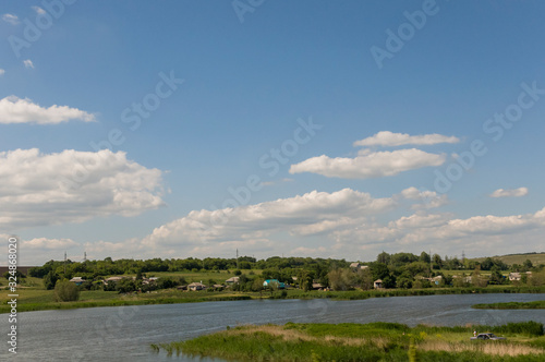 Light white clouds in the warm summer sky over village with small houses far away in the fields. Travelling. People living 