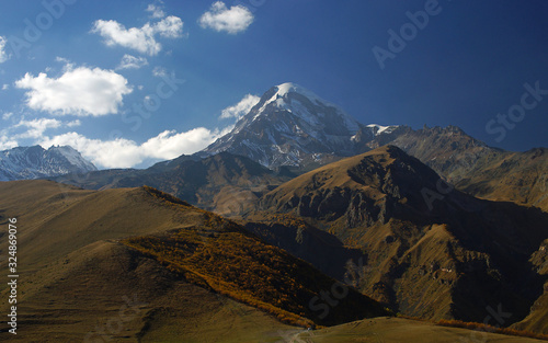 Beautiful sunny view of snowy Mount Kazbegi at autum time. Background of brown mountains and sky, Caucasus, Georgia