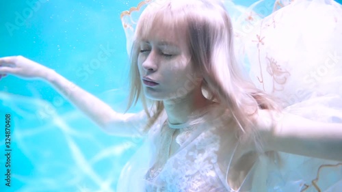 Beautiful blonde girl swims underwater in the pool in a fluffy white dress. Looks like a nymph or a mermaid