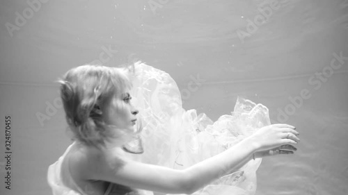Beautiful blonde girl swims underwater in the pool in a fluffy white dress. Looks like a nymph or a mermaid