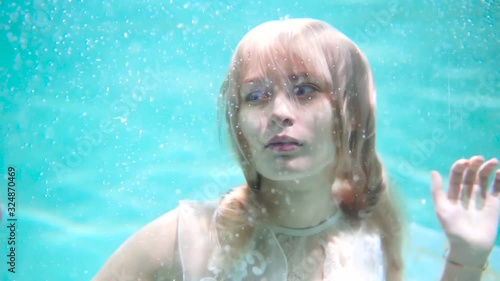 Beautiful blonde girl swims underwater in the pool in a fluffy white dress. Looks like a nymph or a mermaid