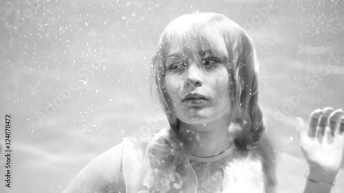 Beautiful blonde girl swims underwater in the pool in a fluffy white dress. Looks like a nymph or a mermaid